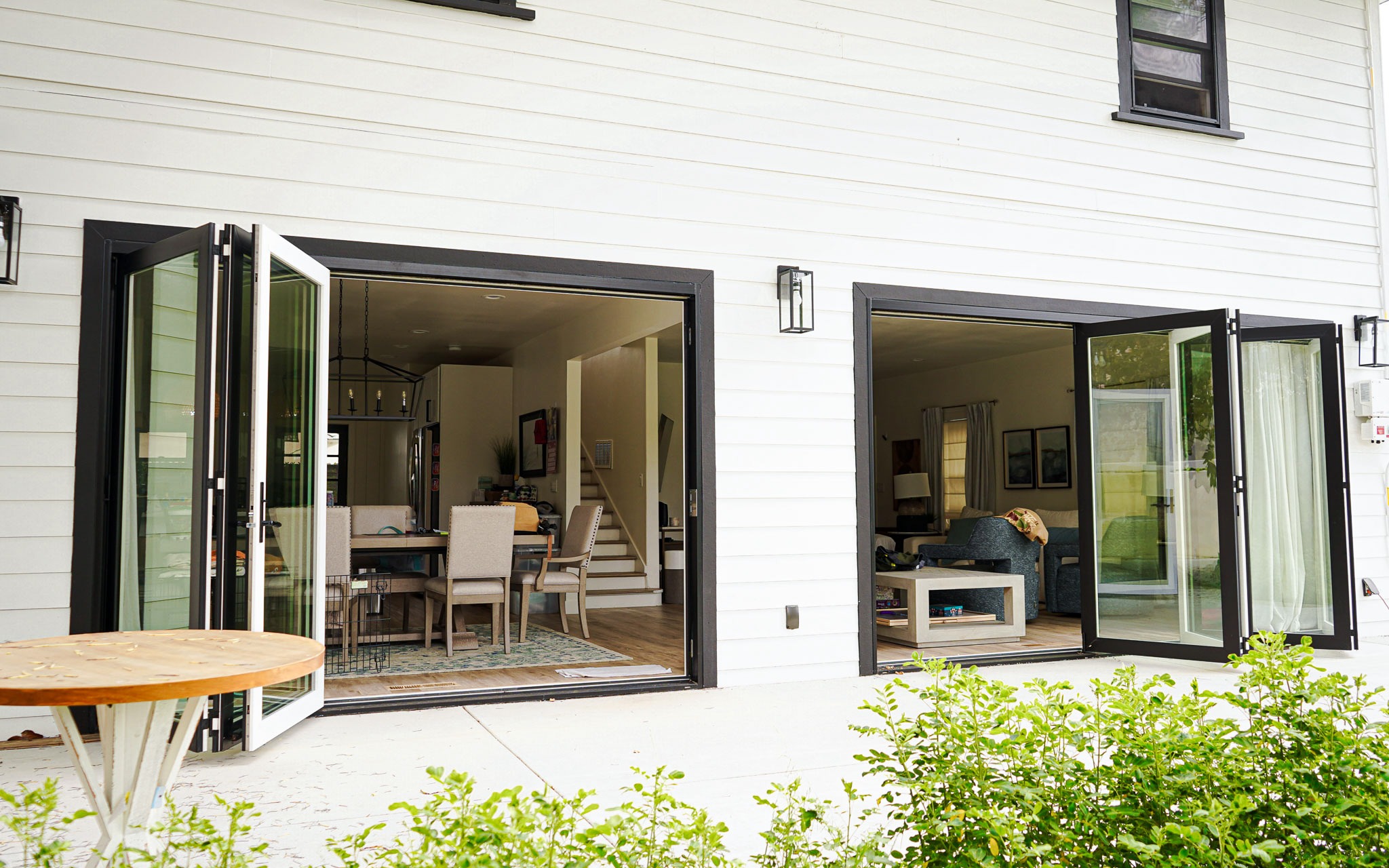 Untitled-79 Modern house with open folding glass doors leading to a stylish living and dining area, viewed from an outdoor patio.