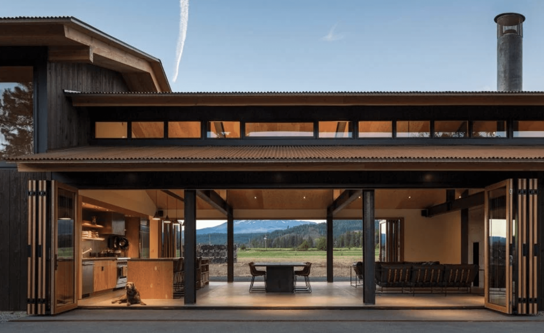 Centor Contemporary house with large sliding glass doors open to an outdoor space. The interior showcases a kitchen and seating area. A view of a landscape with mountains is visible through the doors.