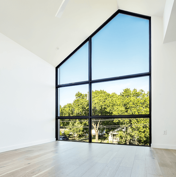 slidingmillgardpopup A room with light wood floors and white walls features large, triangular floor-to-ceiling windows overlooking green trees and a clear blue sky.